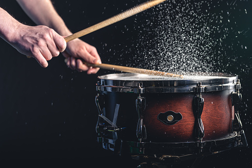 Drummer using drum sticks hitting snare drum with splashing water on black background.