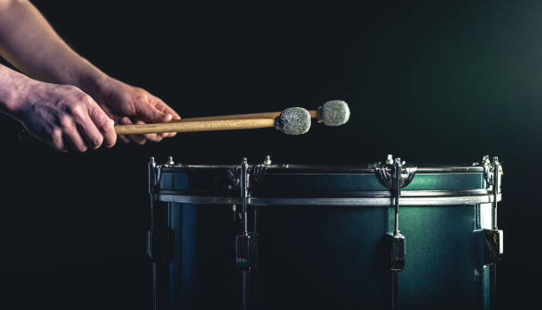 un uomo suona uno strumento a percussione musicale con bastoncini su uno sfondo scuro. - samba dancing dancing drum drumstick foto e immagini stock
