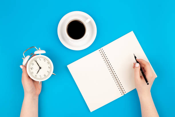 istock Female hands write in a notebook and hold an alarm clock, flat lay. 1481241854