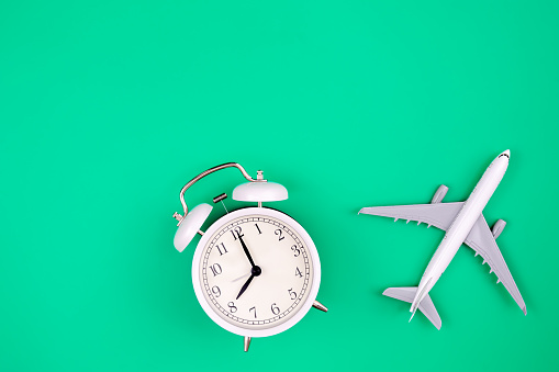 Alarm clock and airplane model on green background, flat lay, copy space.