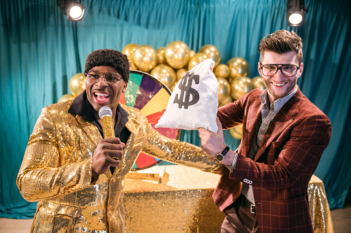 A fun depiction of a competitive TV game show, stylized in late 1970's or early 1980's fashion.  The host, an African American man in a stunning gold blazer, watches as contestants spin a colored wheel to win cash prizes.