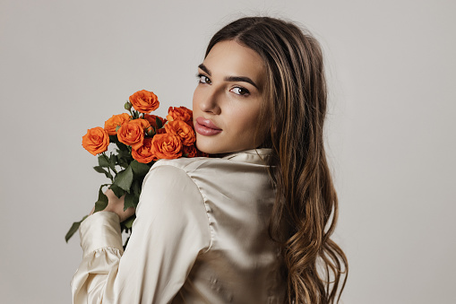 Portrait of a beautiful young woman with long brown hair holding a bouquet of roses, studio photo shot