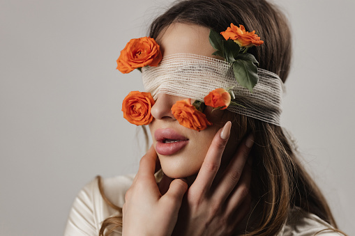 Portrait of a young woman with bandages and fresh roses on her eyes, conceptual studio photo shot