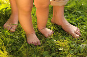 Woman with her child walking barefoot on green grass outdoors, closeup
