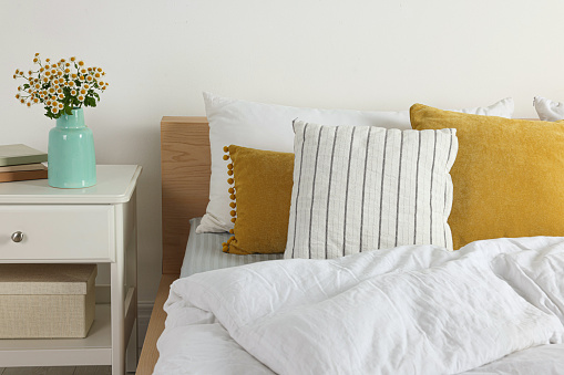 Beautiful room interior with comfortable bed and bouquet of chamomile flowers