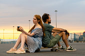 Young pensive couple sitting on longboard back to back with coffee in hands