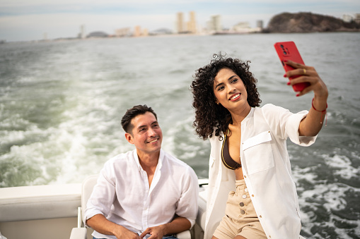 Friends taking a selfie or filming using mobile phone during a yacht trip