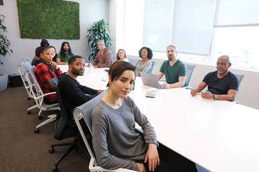 A diverse group of people sitting at a board table and looking at the camera.