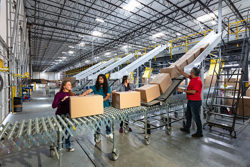 A diverse group of workers handling boxes coming down a conveyor belt in a fulfillment center.