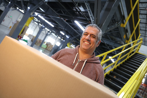 A Middle Eastern man holding a box and smiling near the staircase inside a fulfillment center.