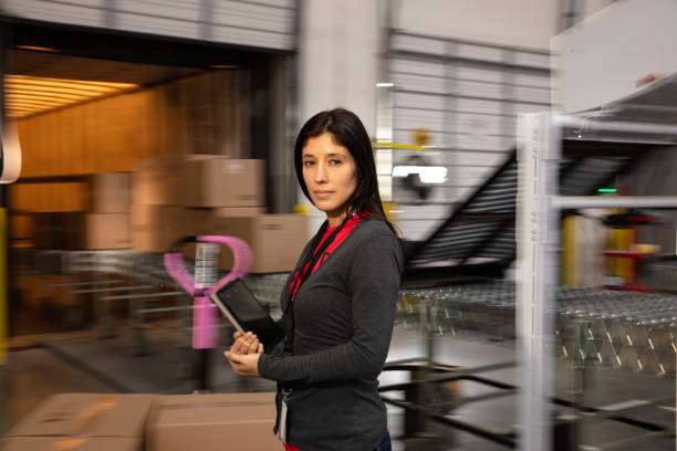 istock Hispanic Woman Holding Digital Tablet And Looking At Camera Standing Next To Cardboard Boxes In a Fulfillment Center 1481252966