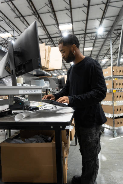 istock Young African American Man Working On a Computer At His Station In a Fulfillment Center 1481253018