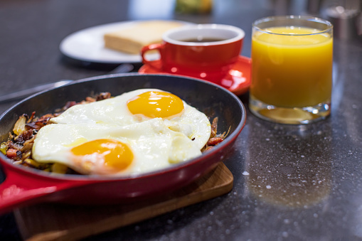 Homemade breakfast skillet with sunny side up eggs, sausages, cup of coffee and orange juice
