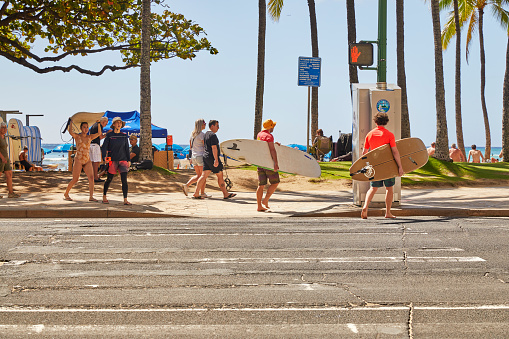 Waikiki, Oahu, Hawaii, USA, - February 6, 2023: People carrying Surfboards while crossing the street at the crosswalk on Kalakaua Avenue