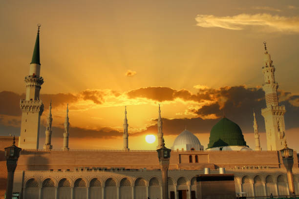 sebuah masjid dengan kubah hijau dan matahari terbenam di belakangnya.  masjid nabi madinah. kubah hijau - masjid nabawi madinah potret stok, foto, & gambar bebas royalti