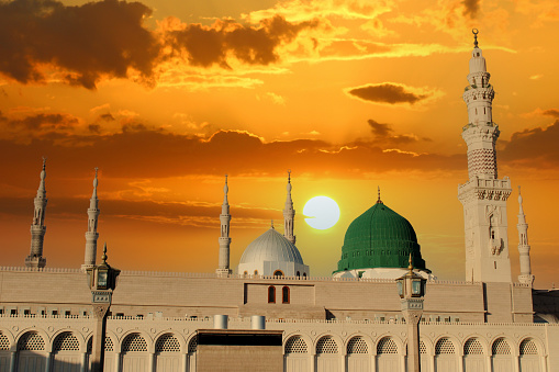 A mosque with a green dome and the sun setting behind it.  Masjid nabi of Medina. Green dome