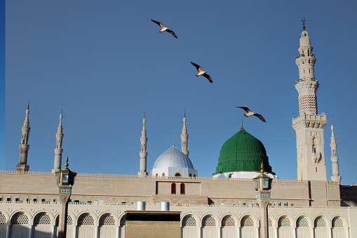 A view of the green dome of a mosque with birds flying in the sky. Masjid nabi of Medina.