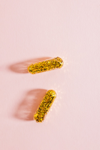 Two pills filled with gold glitter on pink background. Antidepressant concept