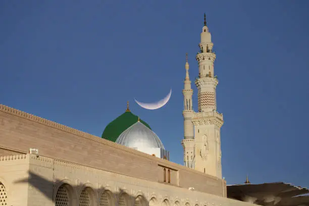 Photo of A mosque with a crescent moon in the sky .Masjid nabi of Medina. Green dome. Ramadan Kareem. Eid Mubarak