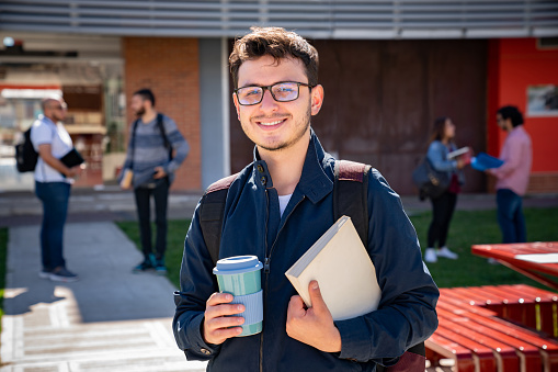 Portrait of a happy Latin American college student carrying a coffee mug and notebooks - education concepts