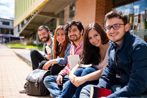 Happy group of students sitting outside a college building and smiling stock photo