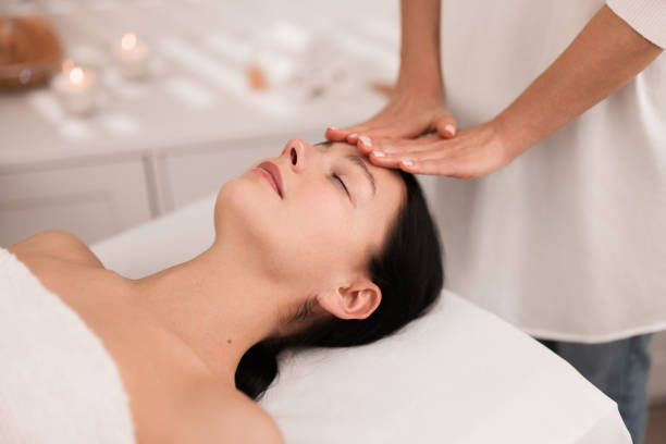 Crop anonymous masseuse doing face massage to female customer in salon