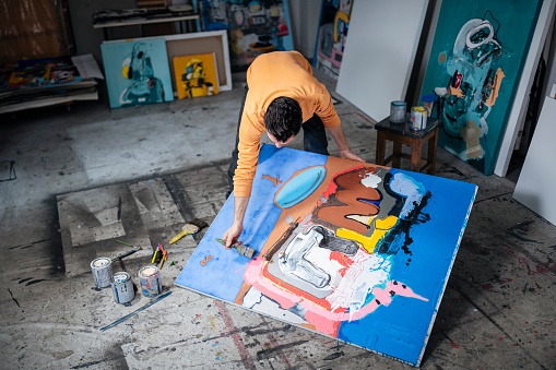 Artist-painter working on painting on the floor in art studio.