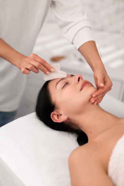 istock Young woman relaxing on couch while beautician massaging face with gua sha 1481267692