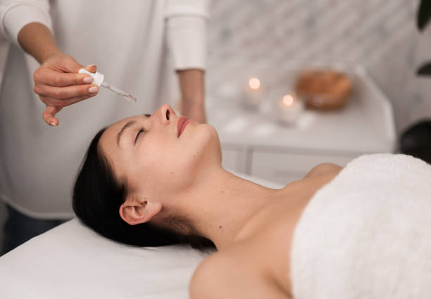 istock Young lady lying with closed eyes while cosmetician applying essential oil on face 1481267704