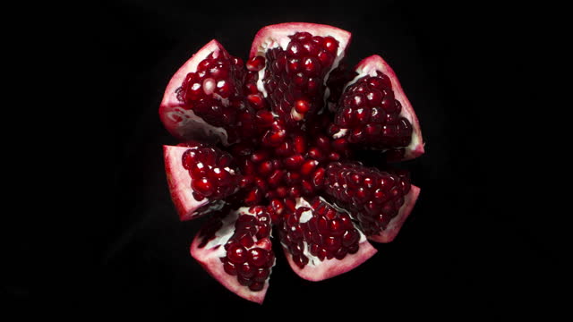 a torn Pomegranate rotates on a black background, red grains, top view.