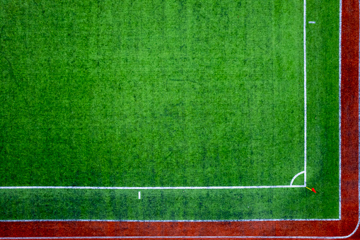Corner point and red corner flag top view in soccer field. Green football carpet field. Drone shot.