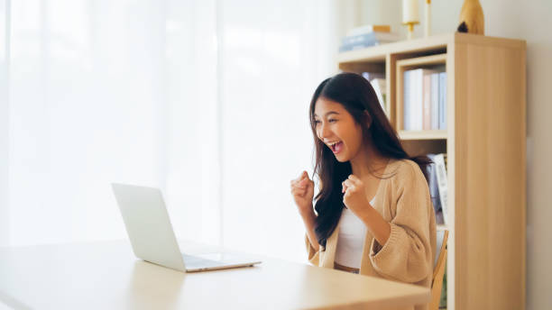 istock Funny euphoric young asian woman celebrating winning or getting e-commerce shopping offer on computer laptop 1481285528