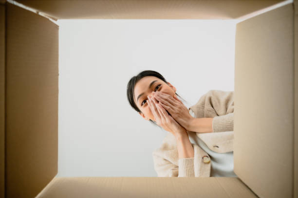 istock Surprised young asian woman unpacking. Opening carton box and looking inside. Packaging box, delivery service. Human emotions and facial expression 1481285603