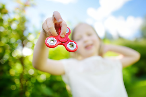 Cute school girl playing with colorful fidget spinner on the playground. Popular stress-relieving toy for school kids and adults.