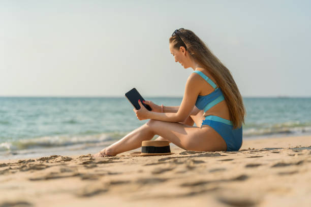 istock Digital nomad workcation at the beach. Beautiful caucasian woman in bikini using her digital tablet to work with her team and communicate with her friends happily on the beach 1481287828