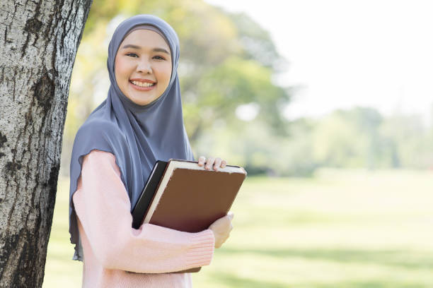 Asian young muslim woman wear hijab holding book with happiness feeling, smiling in park. Education concept Asian young muslim woman wear hijab holding book with happiness feeling, smiling in park. Education concept religious islam book stock pictures, royalty-free photos & images