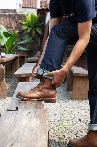 Men wearing leather boots and blue denim jeans standing on the wood chair