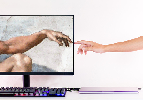 A person's hand touching a computer recreating Michelangelo's The Creation of Adam.  Artificial intelligence and machine learning concept.