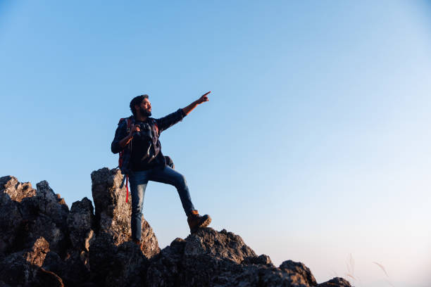 istock Asian backpacker on mountain peak and pointing to sky 1481299260