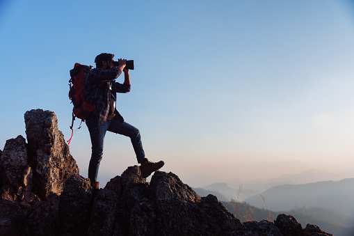 Asian backpacker on mountain peak and using binoculars looking forward