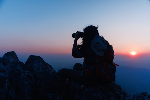 Asian woman backpacker on mountain peak and using binoculars