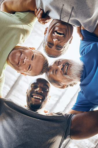 Low angle, portrait or fitness huddle of men in workout gym, training exercise or healthcare wellness in bonding. Happy friends, mature or hug in sports teamwork, collaboration or diversity community