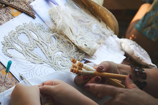 Close-up photo of a woman and a girl making lace using bobbins