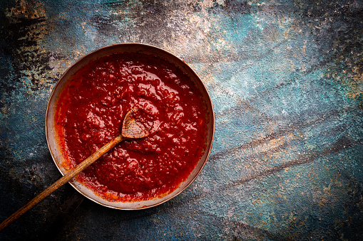 Classic homemade Italian tomato sauce with basil for pasta and pizza in the pan on blue background, top view.