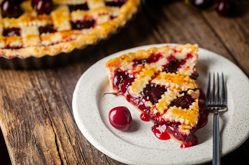 piece of Delicious homemade classic cherry pie with a flaky crust on dark rustic background