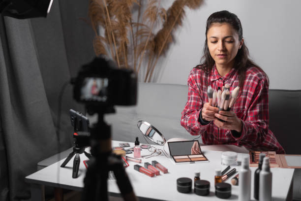 istock Beauty blogger or vlogger filming daily make-up routine tutorial on camera, showing make up brushes. Influencer girl livestreaming cosmetics product review in home studio. 1481309330