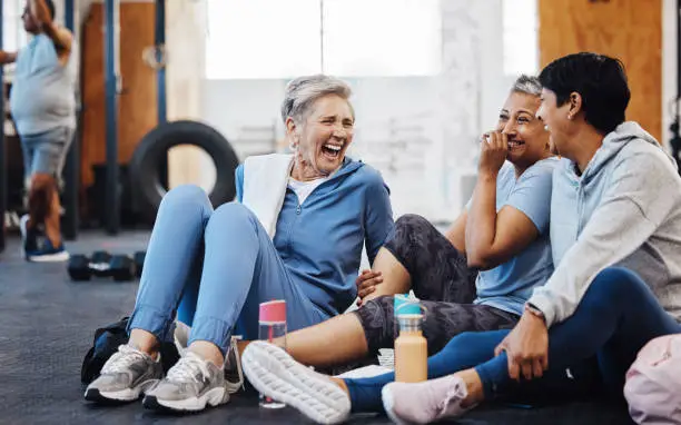 Photo of Gym, laughing and group of mature women telling joke after fitness class, conversation and comedy on floor. Exercise, bonding and happy senior woman with friends sitting chatting together at workout.