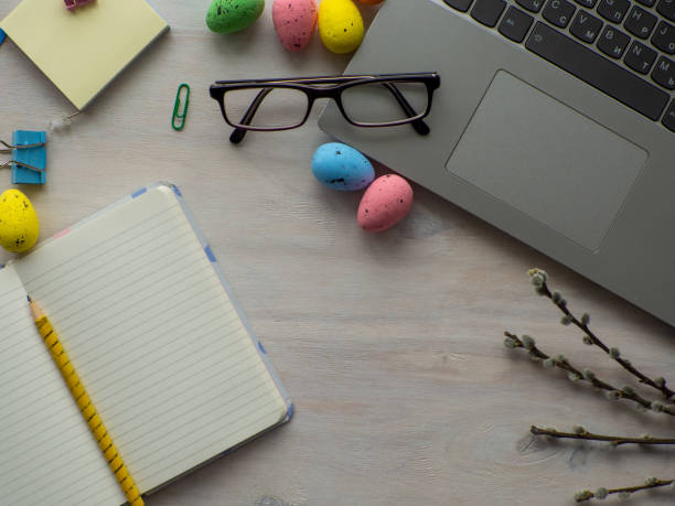 istock Work desk with devices and easter holiday multicolored eggs on wood background 1481312830