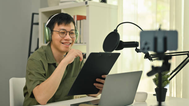 istock Smiling young man radio host wearing headphone streaming his live podcast using professional microphone at his broadcast studio. 1481313829