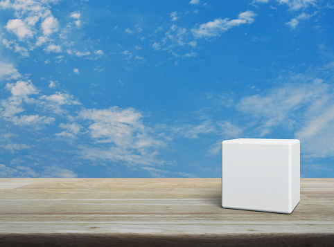White block cubes on wooden table over blue sky with white clouds